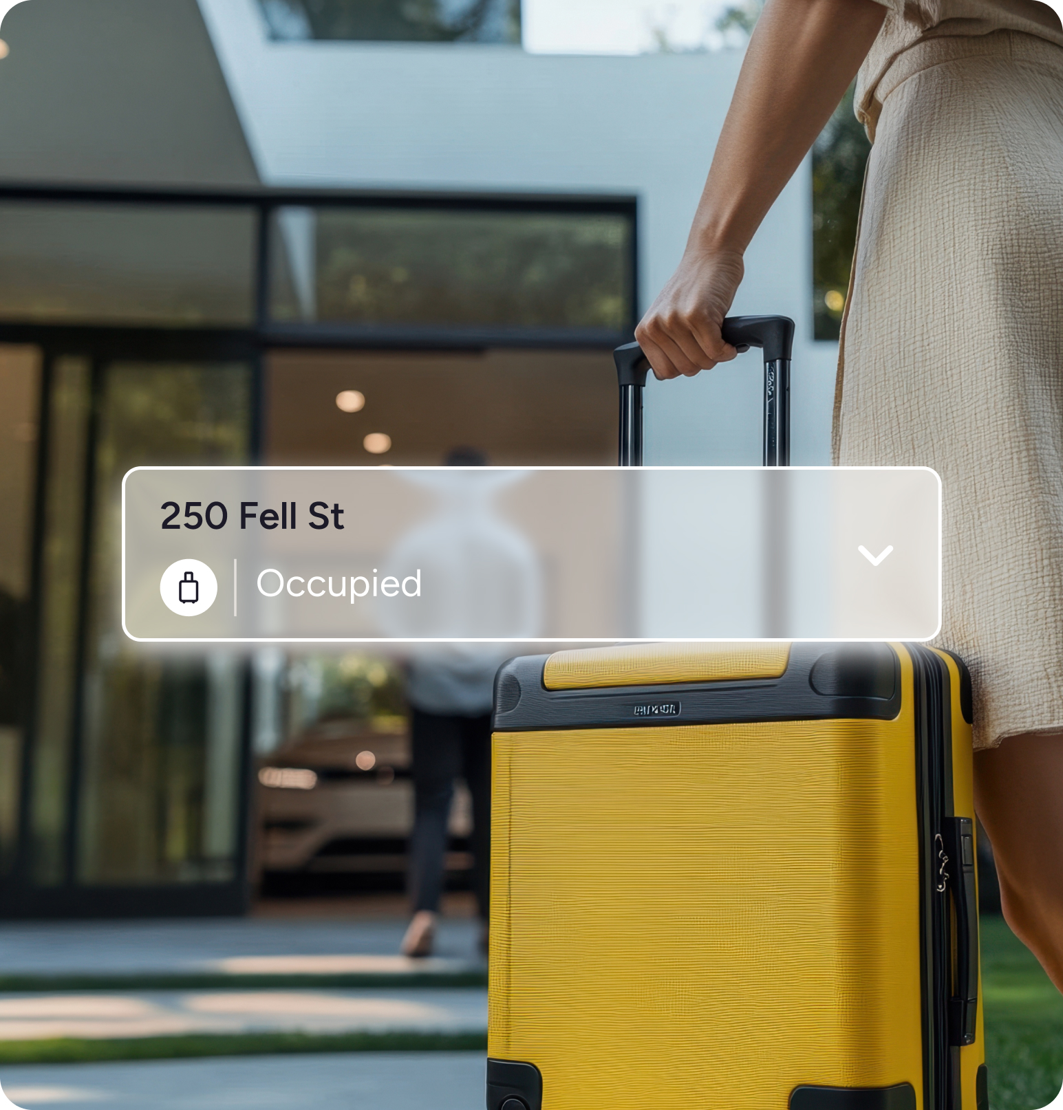 Person holding the handle of a yellow suitcase outside a modern house with a person walking toward the entrance, with an overlay showing '250 Fell St' and 'Occupied' status.