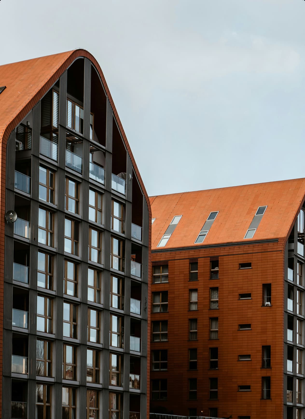 Modern residential buildings with orange sloped roofs and large glass windows under a cloudy sky.