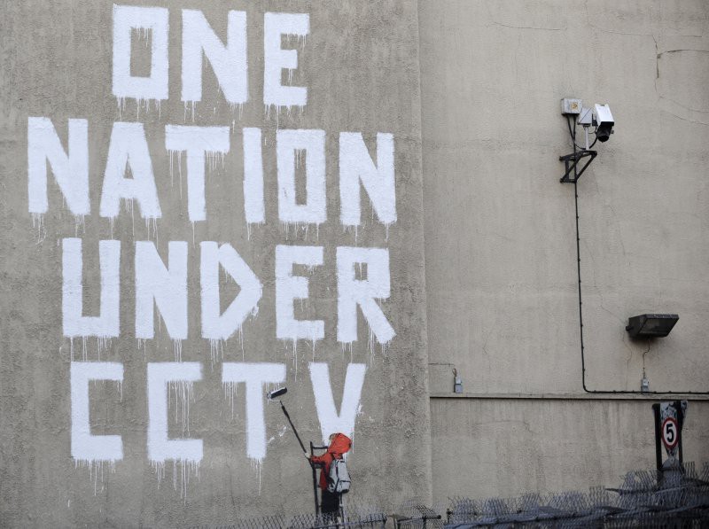 A mural with the words ONE NATION UNDER CCTV next to a CCTV camera