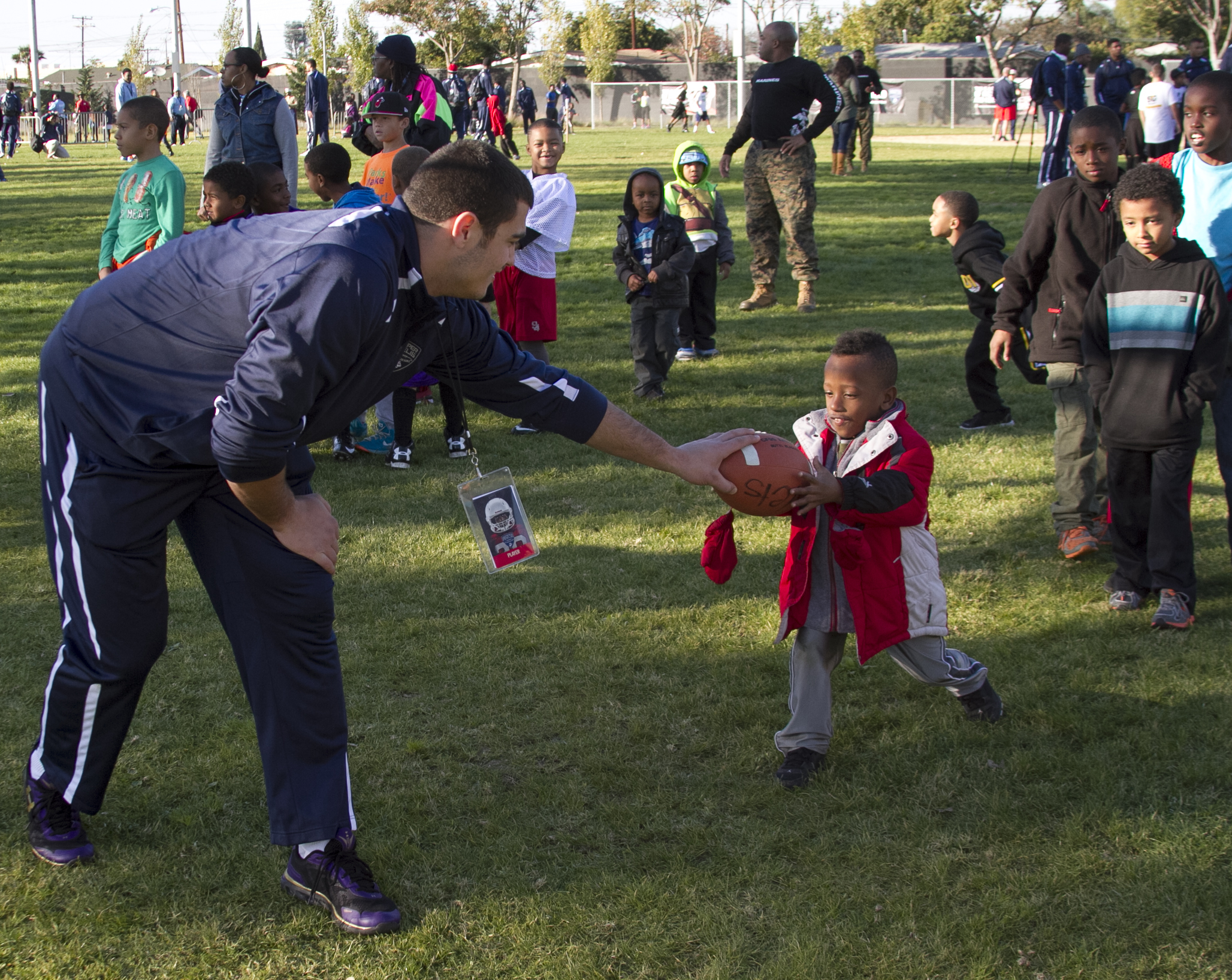 Student-athlete hands a football to a young fan during a community event, representing athlete influence built on authentic community trust.