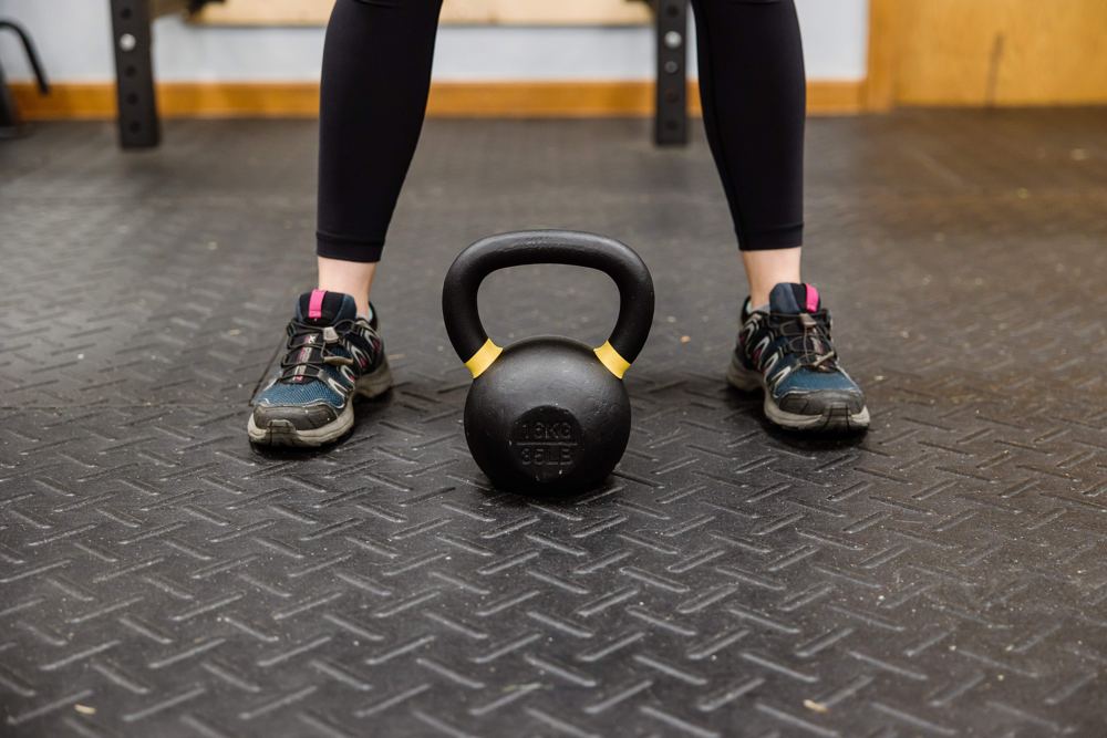 Athlete in training shoes standing behind a kettlebell on a gym floor