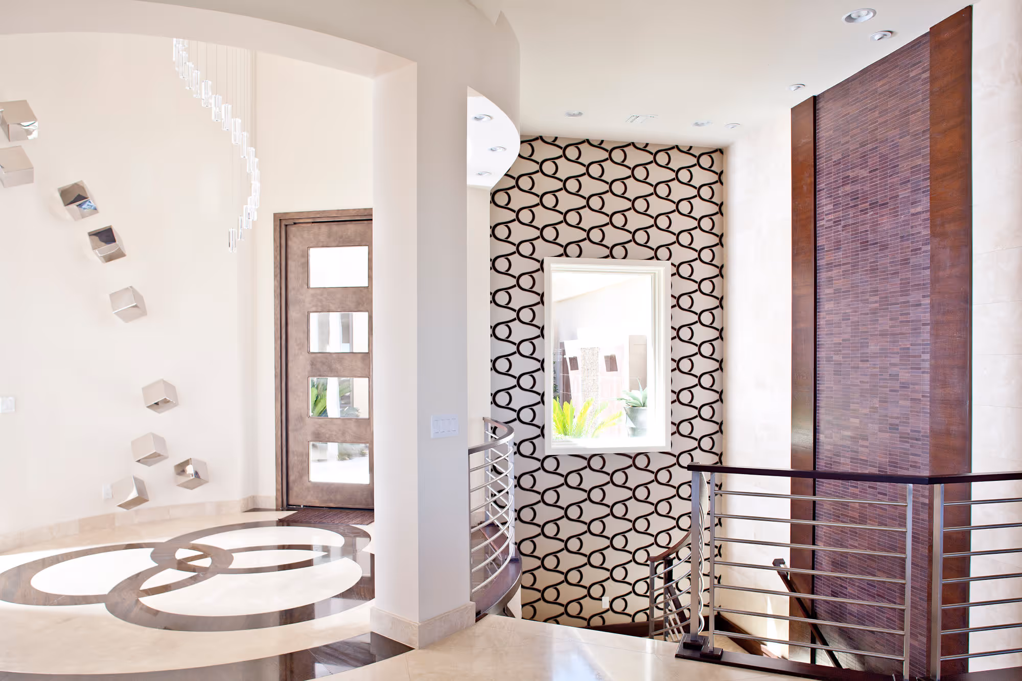 Modern custom home entry with pivotal front door, wallpaper, stone wall and modern crystal light. 