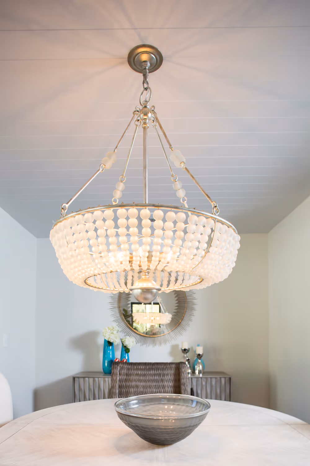 Dining room with white walls, galls white chandelier, shiplap ceiling and round gold wall mirror.