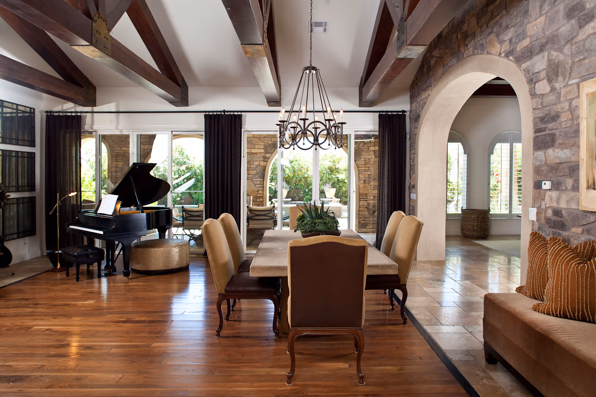 Spanish styled dining room with wood ceiling trusses, wood flooring, black wrought iron chandelier.