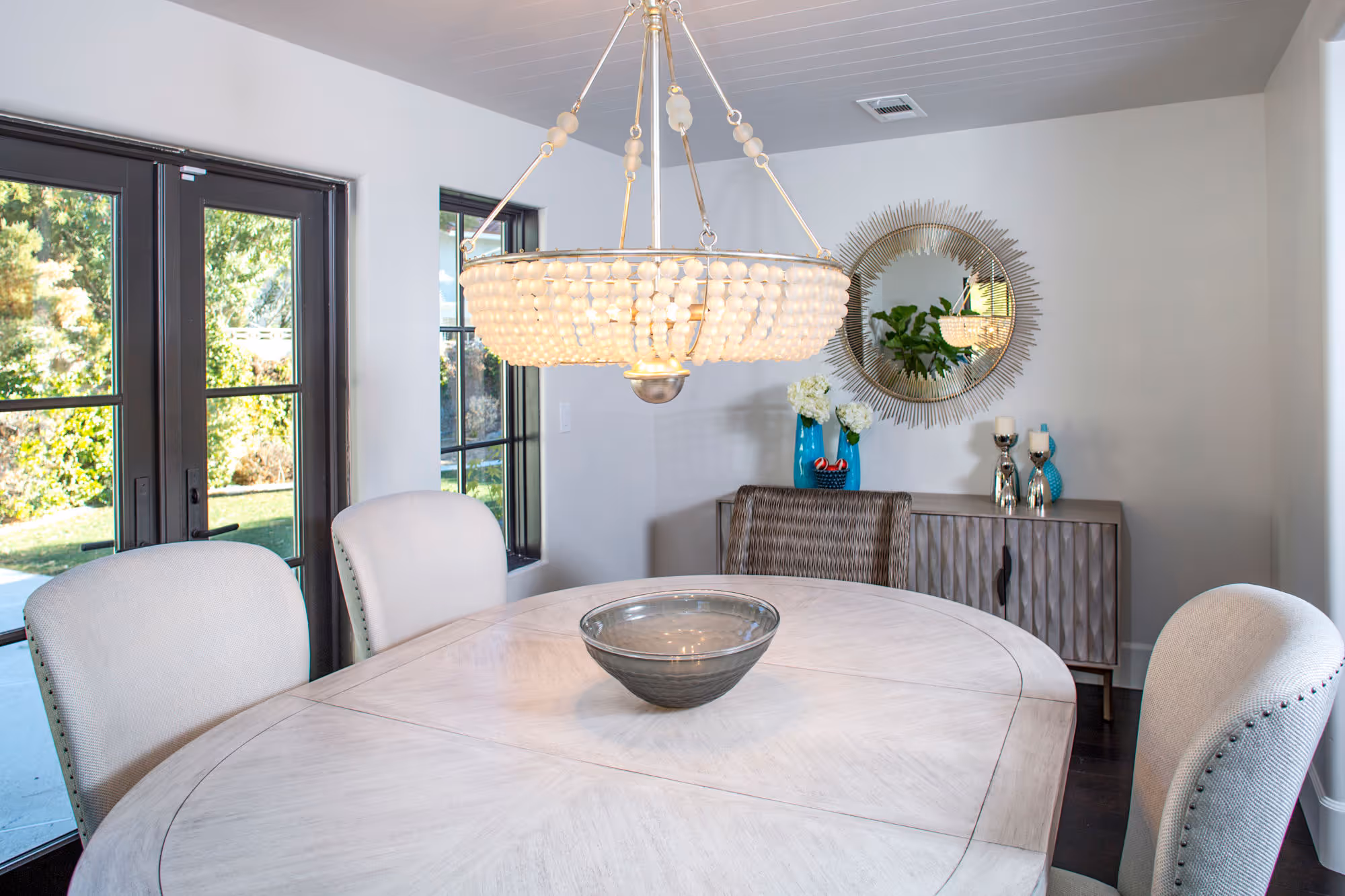 Dinning area, chandelier, shiplap ceiling with white wash wood table upholstered chairs.