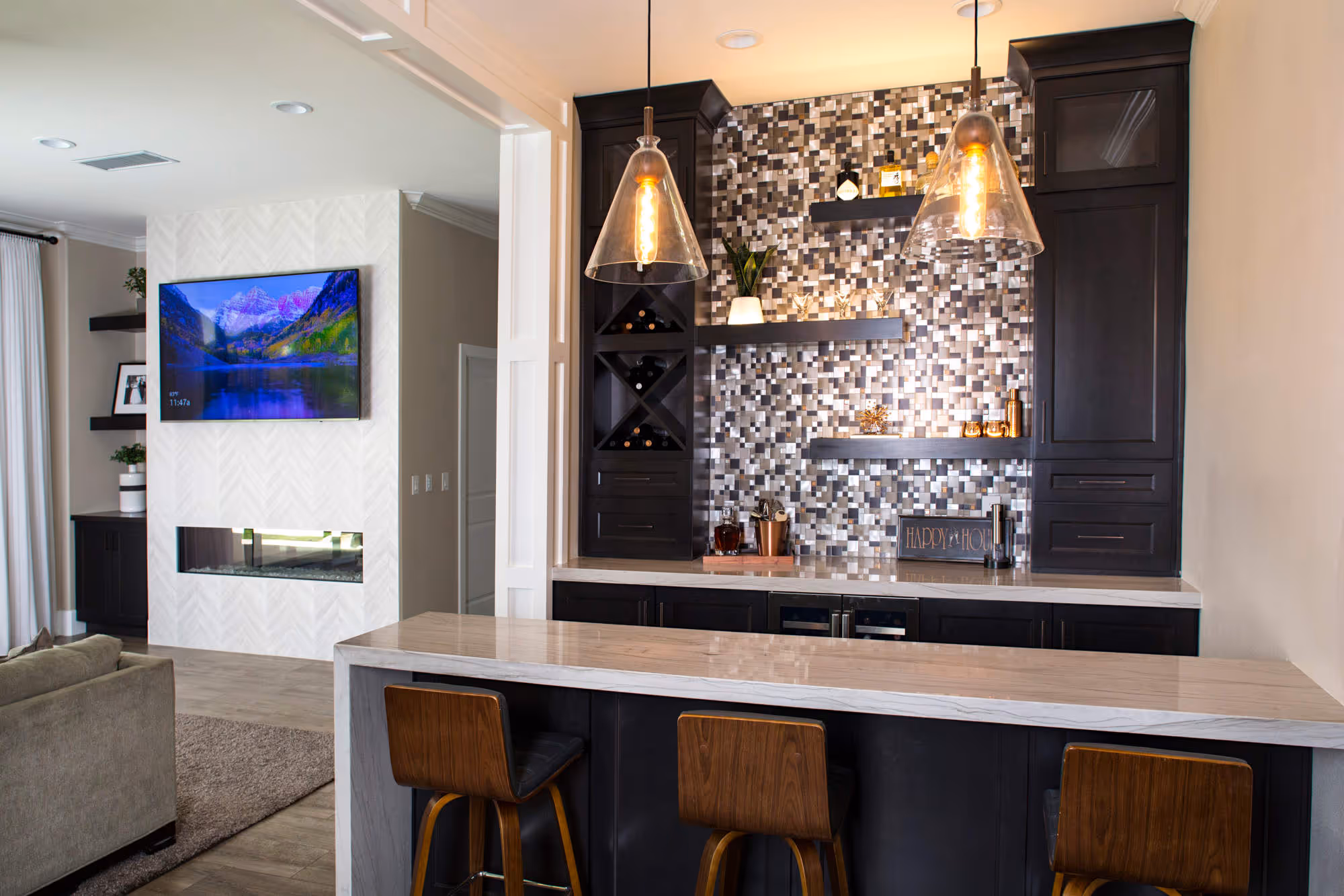 Family room with titled fireplace wall and bar section with barstools and pendent lighting.
