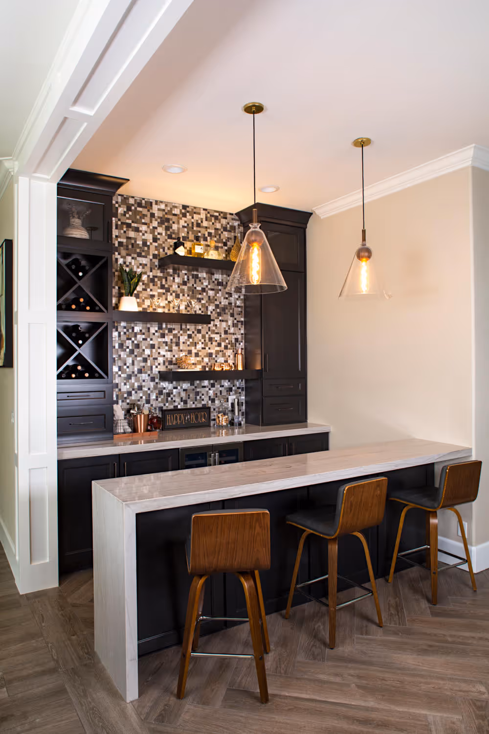 Home bar with barstools, natural stone bar top, pendent lights, dark cabinets.
