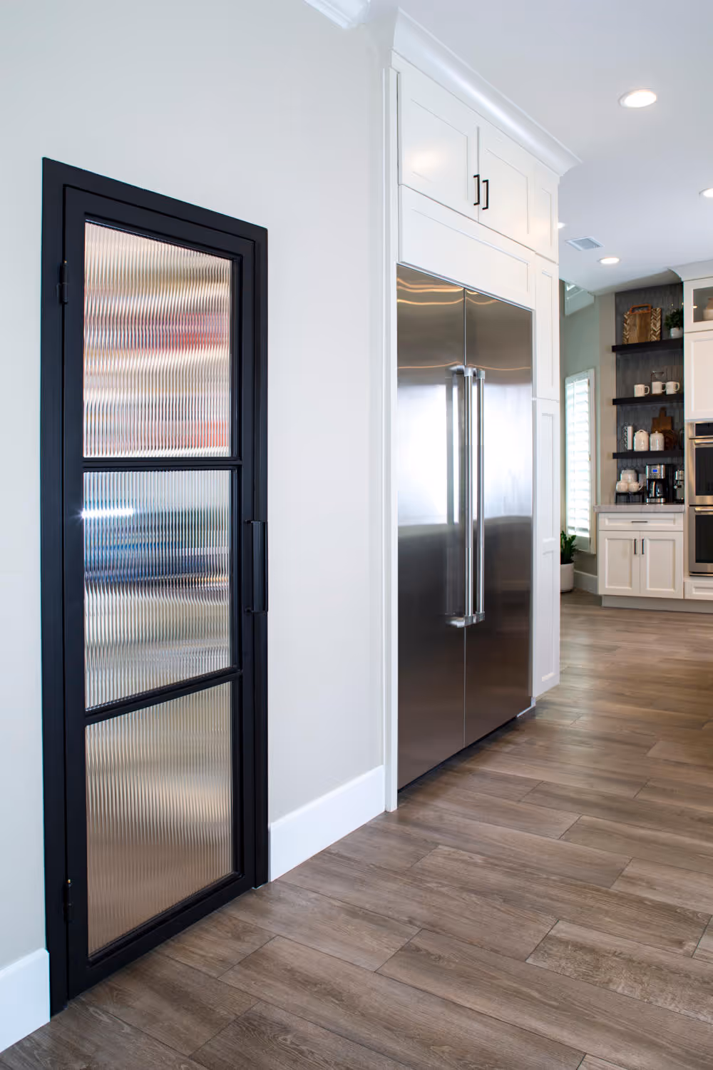 Black iron and reed glass pantry door next to Sub Zero refrigerator in white kitchen.