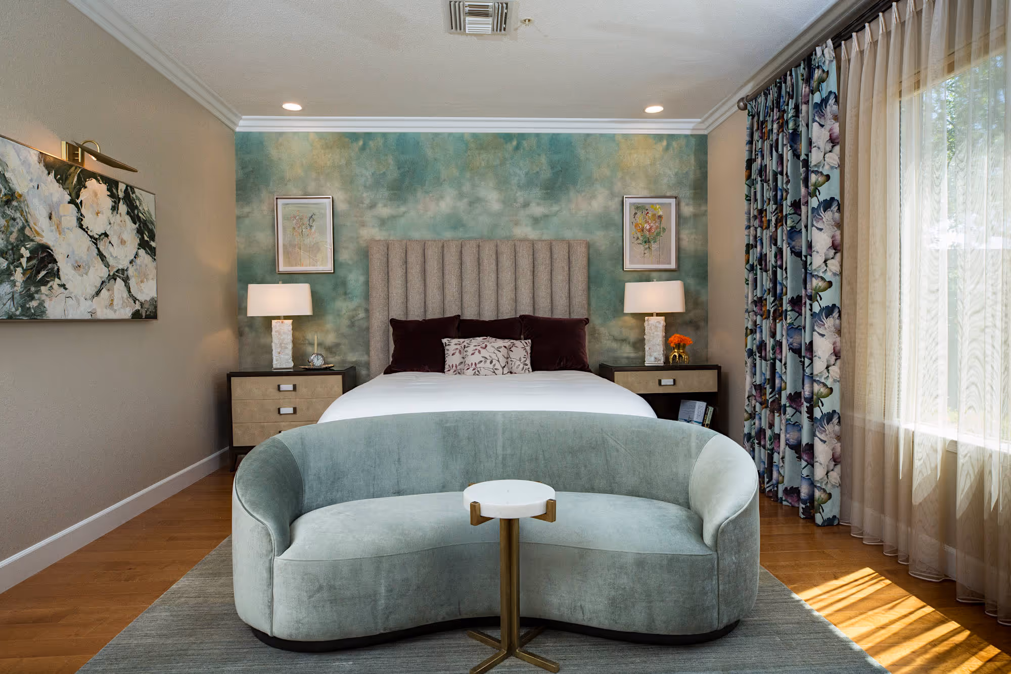 Master bedroom with sage wallpaper, multi colored drapes with sheers, wood floor, curved sofa.