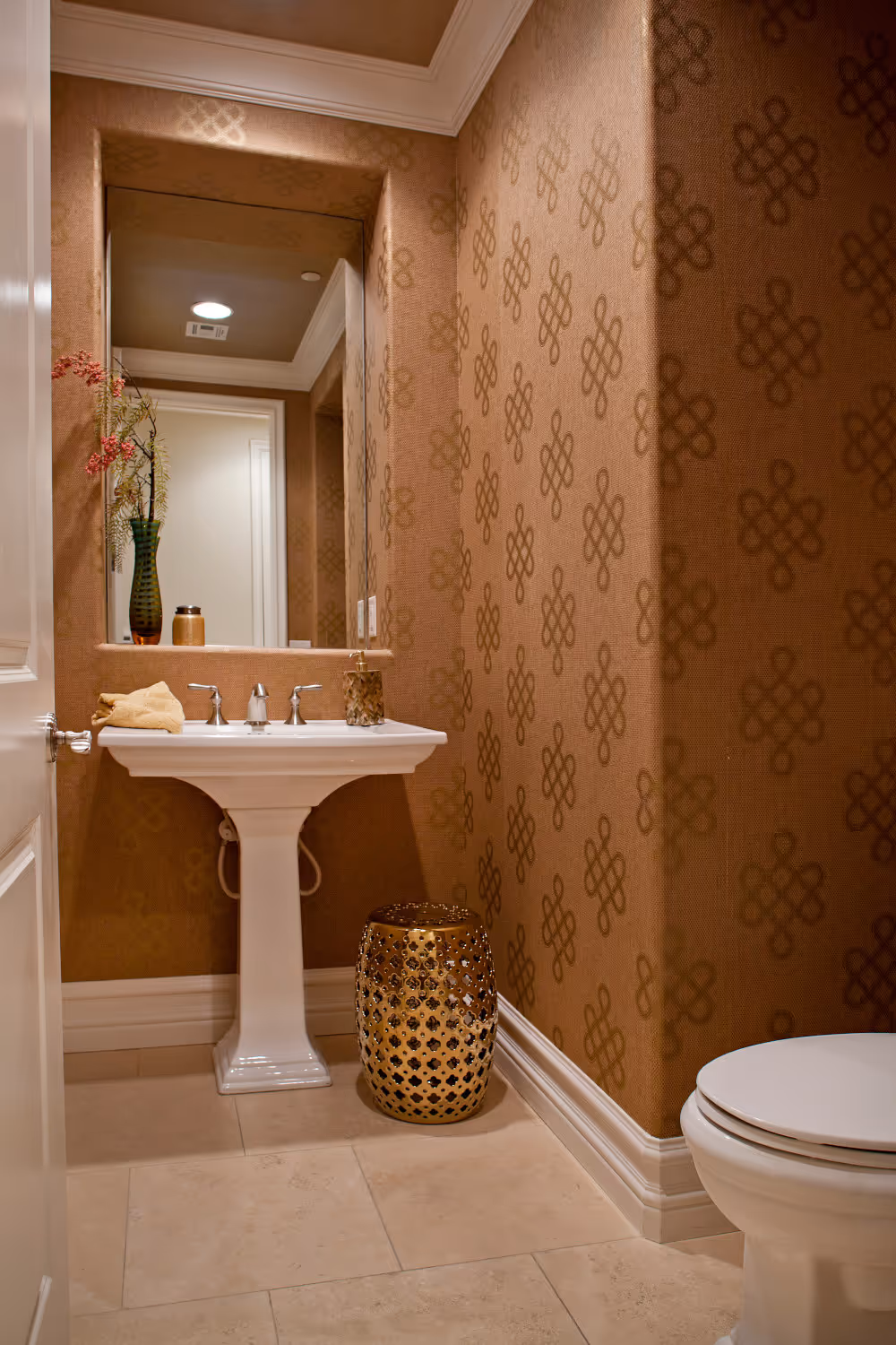 Copper grass cloth wallpaper powder bath with white pedestal sink and recessed mirror.