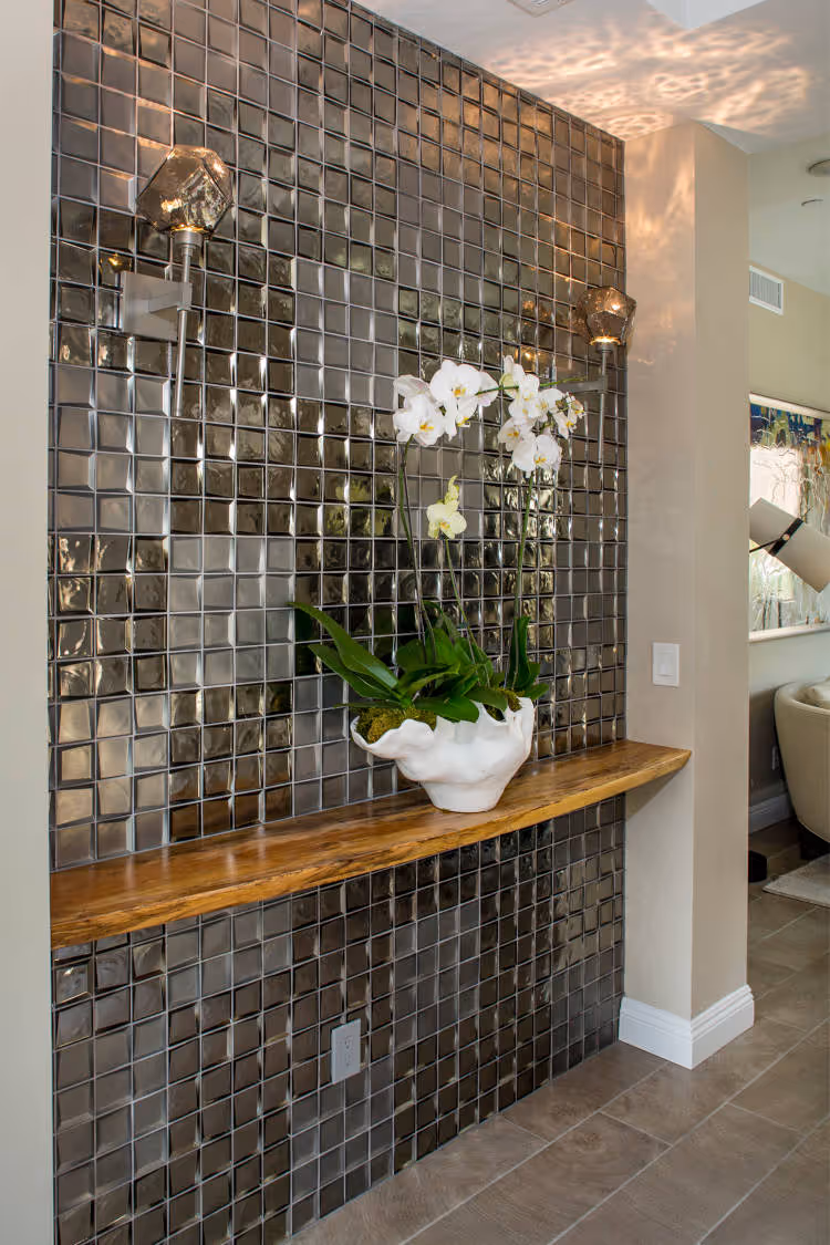 Home entry with glass tile on wall and wooden shelf.