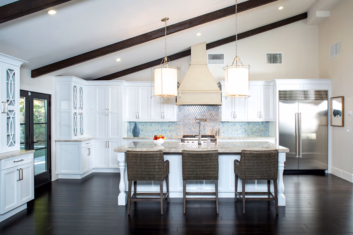 Santa Barbara styled white kitchen, wood ceiling beams, large island with woven reed counter stools.