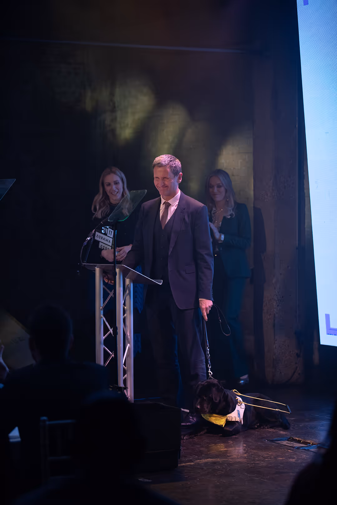 Lord Holmes of Richmond and his guide dog, Nancy on stage accepting the award for Most progressive regulation on behalf of the Electronic Trade Documents Act 2023