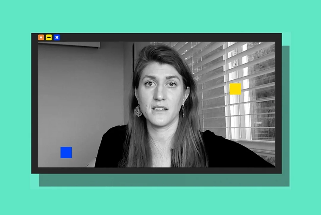 A woman with long hair is speaking in a video call, shown in black and white, against a colorful background with window blinds.