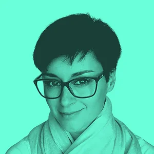 A person with short hair and glasses, wearing a light scarf, smiles against a bright turquoise background.