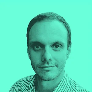 Portrait of a man with short hair, wearing a striped shirt, against a bright turquoise background.