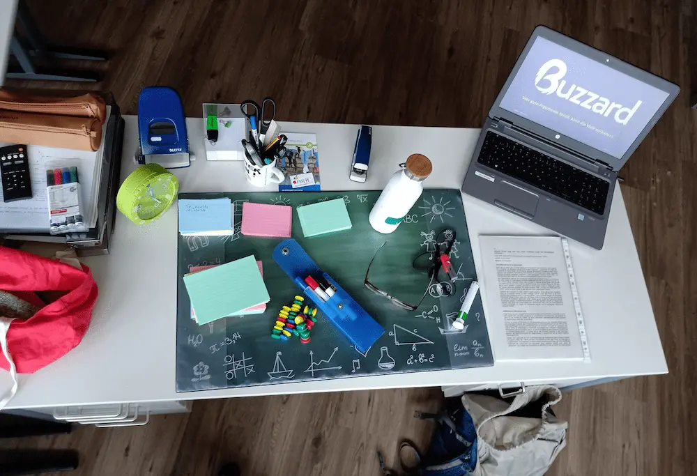 Schultisch mit Lernmaterial und Buzzard auf dem Laptop