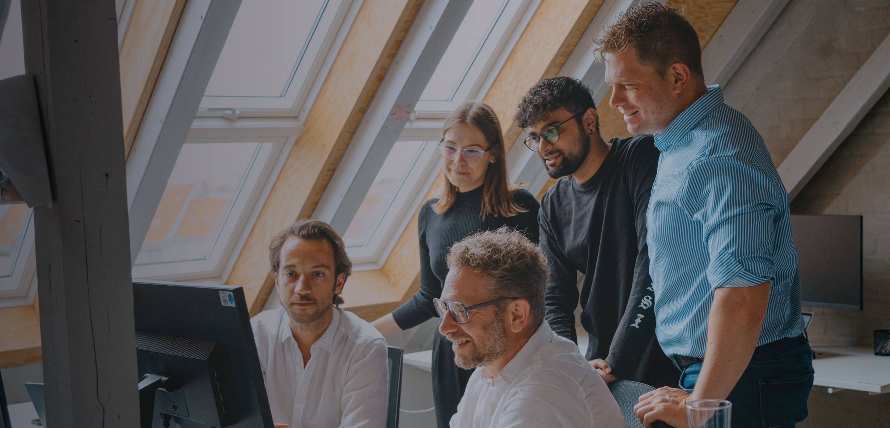 A diverse group of professionals standing around a computer, collaborating and discussing digital coaching solutions with Sharpist.