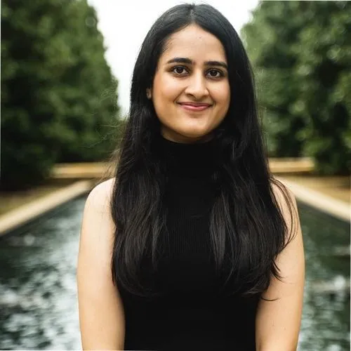 Smiling woman with long black hair wearing a black sleeveless top standing in front of a water feature and greenery.