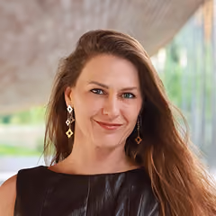 Smiling woman with long brown hair wearing geometric earrings and a dark sleeveless top.