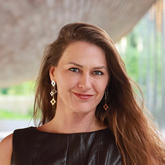 Smiling woman with long brown hair wearing geometric earrings and a dark sleeveless top.