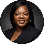 Portrait of a smiling Black woman wearing gold hoop earrings and a black blazer with a dark grey background.
