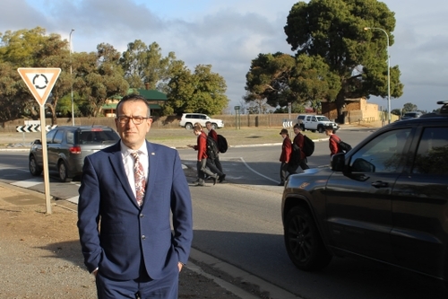 Mr Piccolo at the intersection with students dodging cars to cross the road in the background.