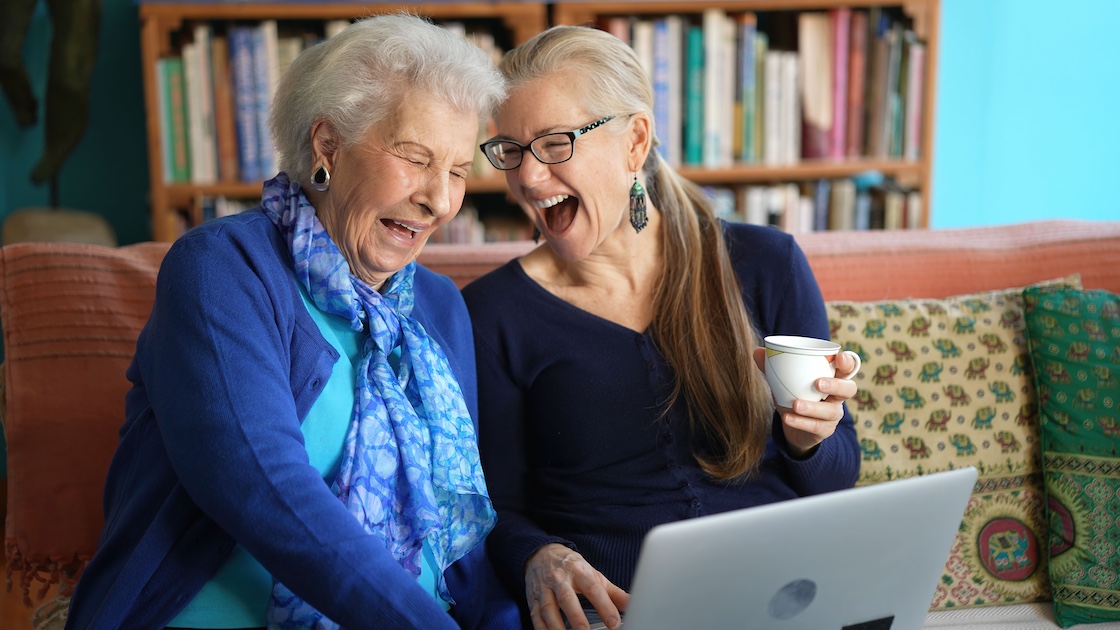 elderly woman and adult daughter looking at laptop and laughing