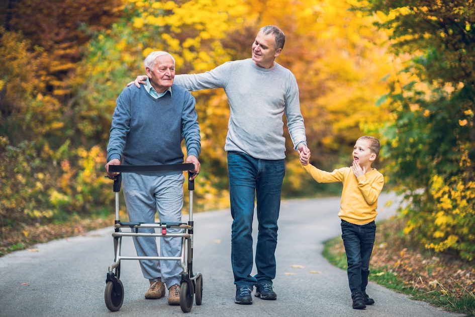 Grandfather walking with a walker next to his son and grandson outside