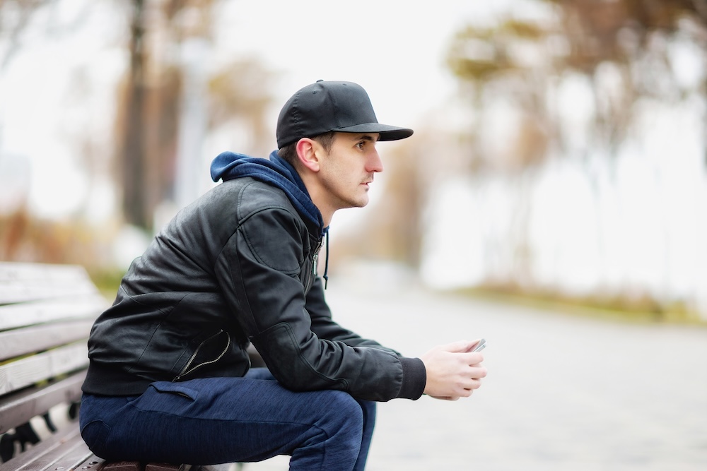 man with a hat on sitting on a park bench looking forward