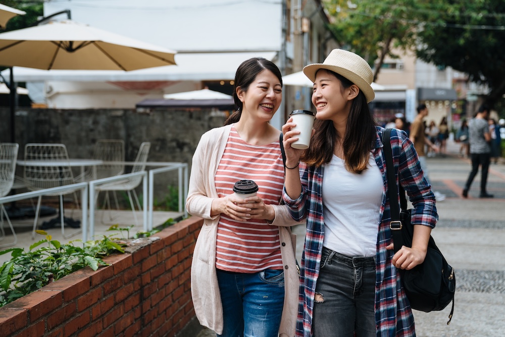 two friends walking outdoors smiling with coffee