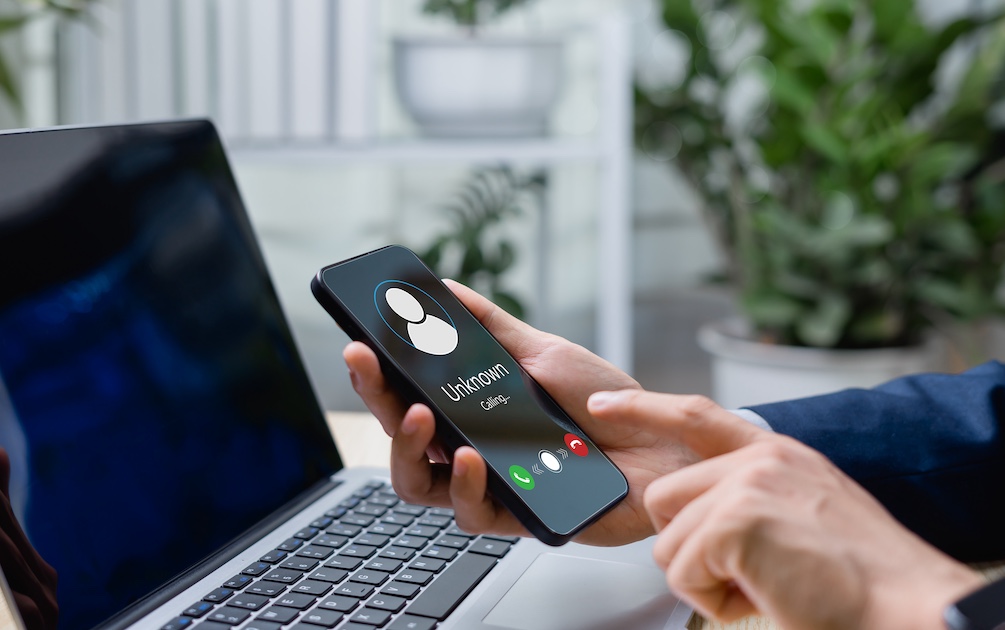 hand holding cell hone with unwanted call near a computer screen