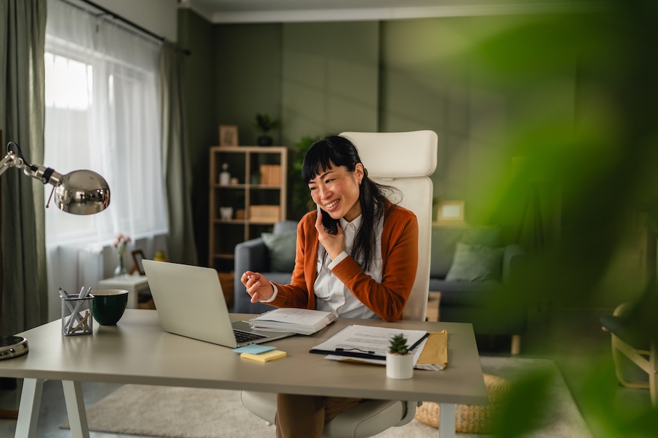 Smiling asian woman middle age talking on phone at her desk