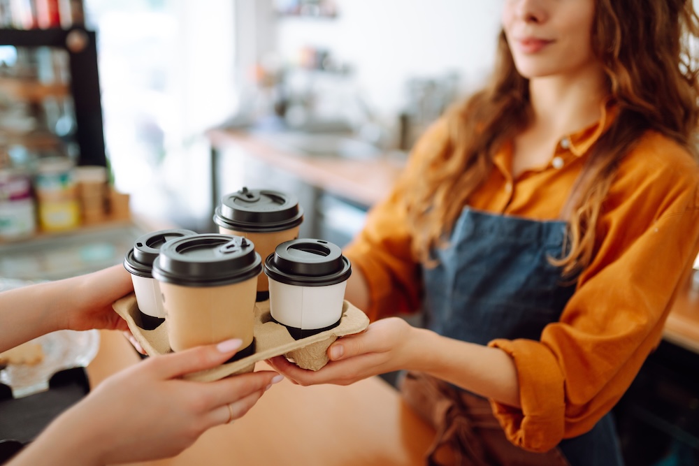 coffee shop worker handing tray of coffee to customer