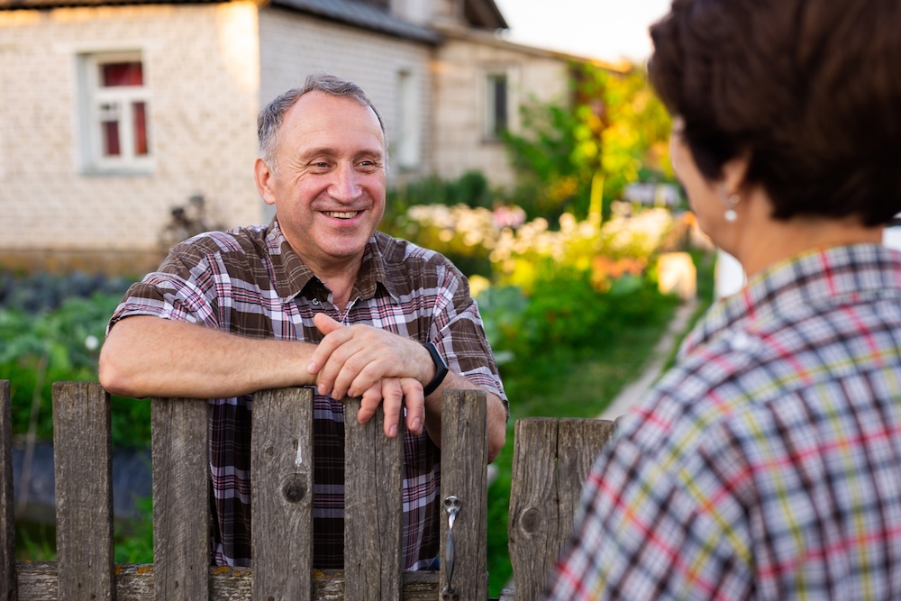man talking to someone outside leaning on a fence