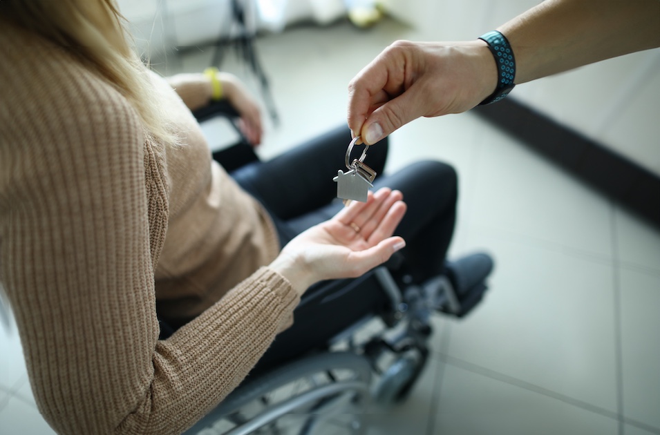 zoomed out image of a house key handoff to a woman sitting in a wheelchair