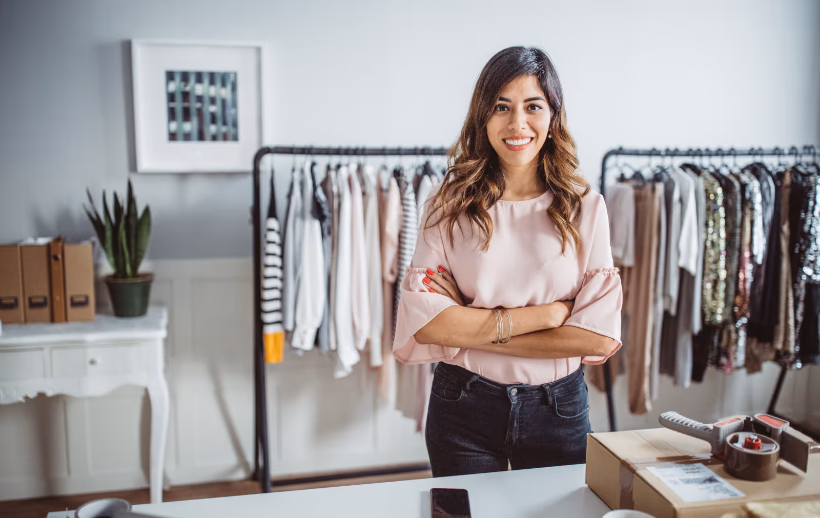 A fashion executive stood with their arms folded in a brand showroom, with garments behind and a parcel on the table