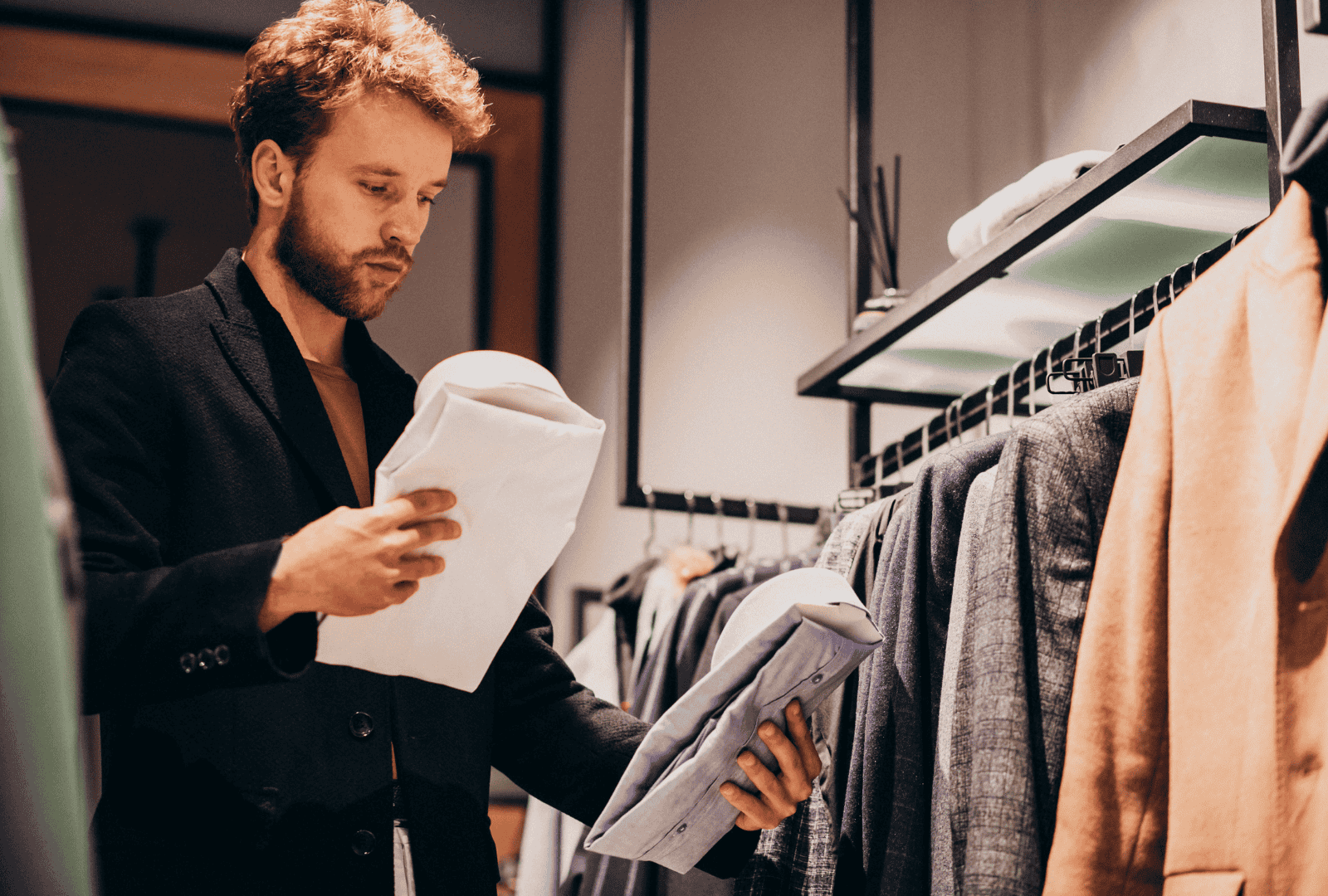 A buyer wearing a black wool blazer is comparing two shirts side by side to complete a collection