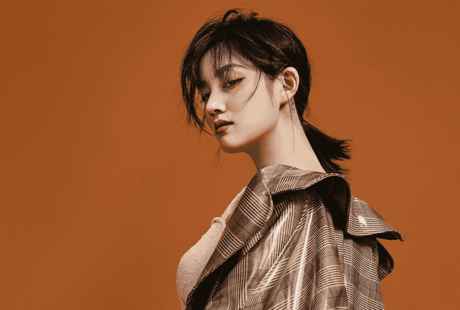 Asian model posed looking back at the camera, wearing a pvc-style luxury brown long coat.