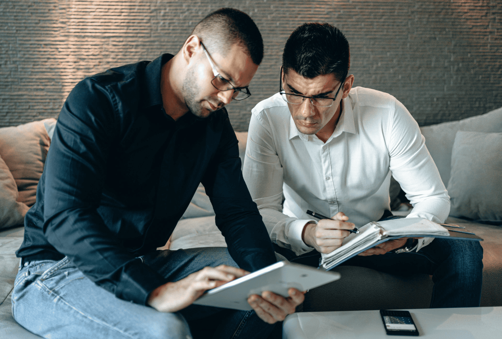 Two executives looking at digital tool options on an iPad and making notes on a notepad