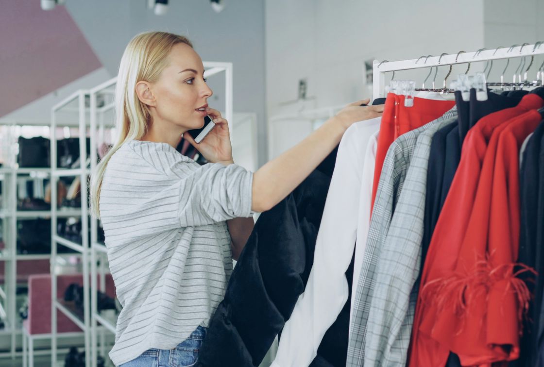 A woman speaking on the phone near some clothing.