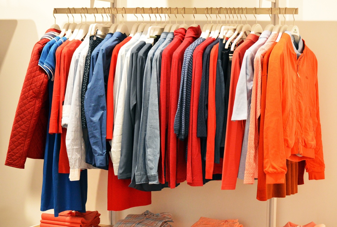 A mix of brightly colored jackets, shirts and t-shirts on a clothing rack