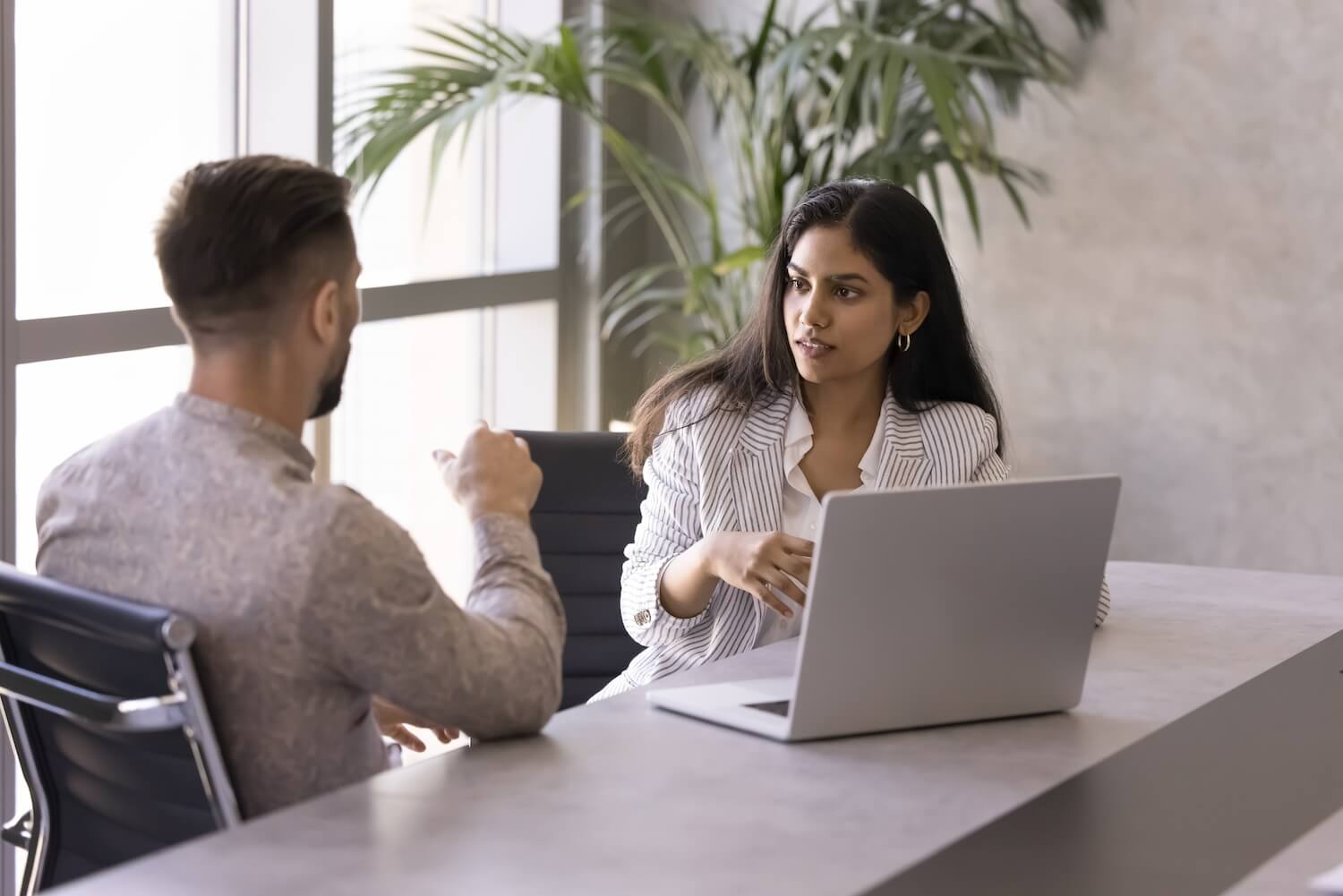 Manager und Mitarbeitende besprechen konstruktives Feedback in einem modernen Büro mit Laptop.