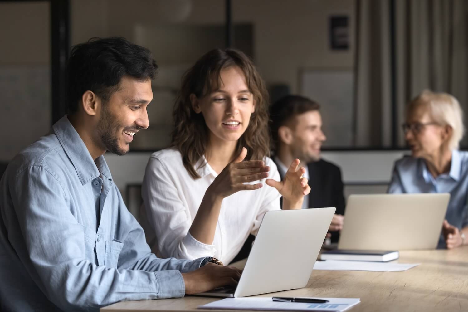 Employees collaborating around a laptop in a workshop setting, representing data-driven measuring B2B coaching success and learning outcomes.