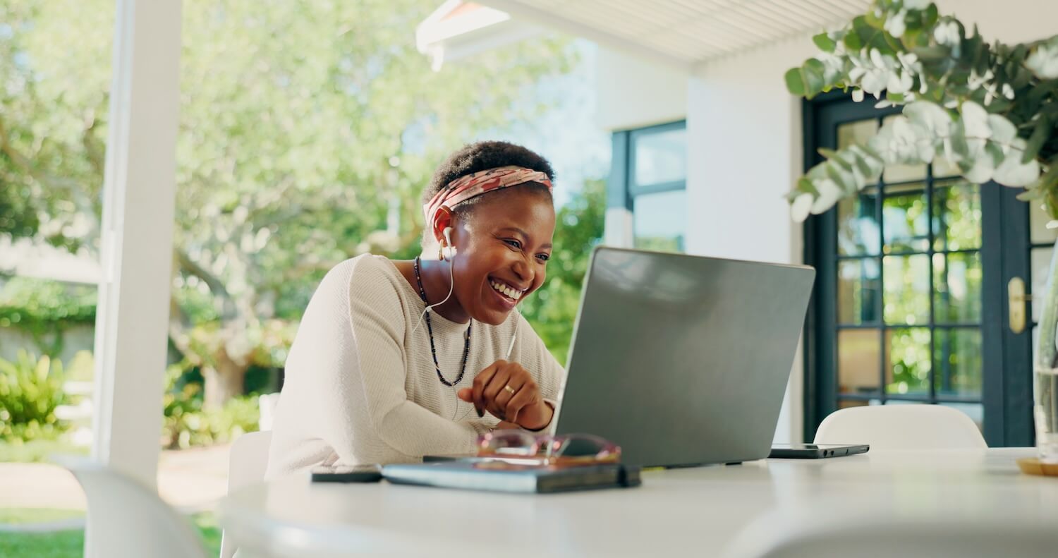 Lächelnder Fachmann, der zu Hause an einem Laptop arbeitet und damit Remote-Führung und produktives Arbeiten aus der Ferne in einer entspannten Umgebung veranschaulicht.