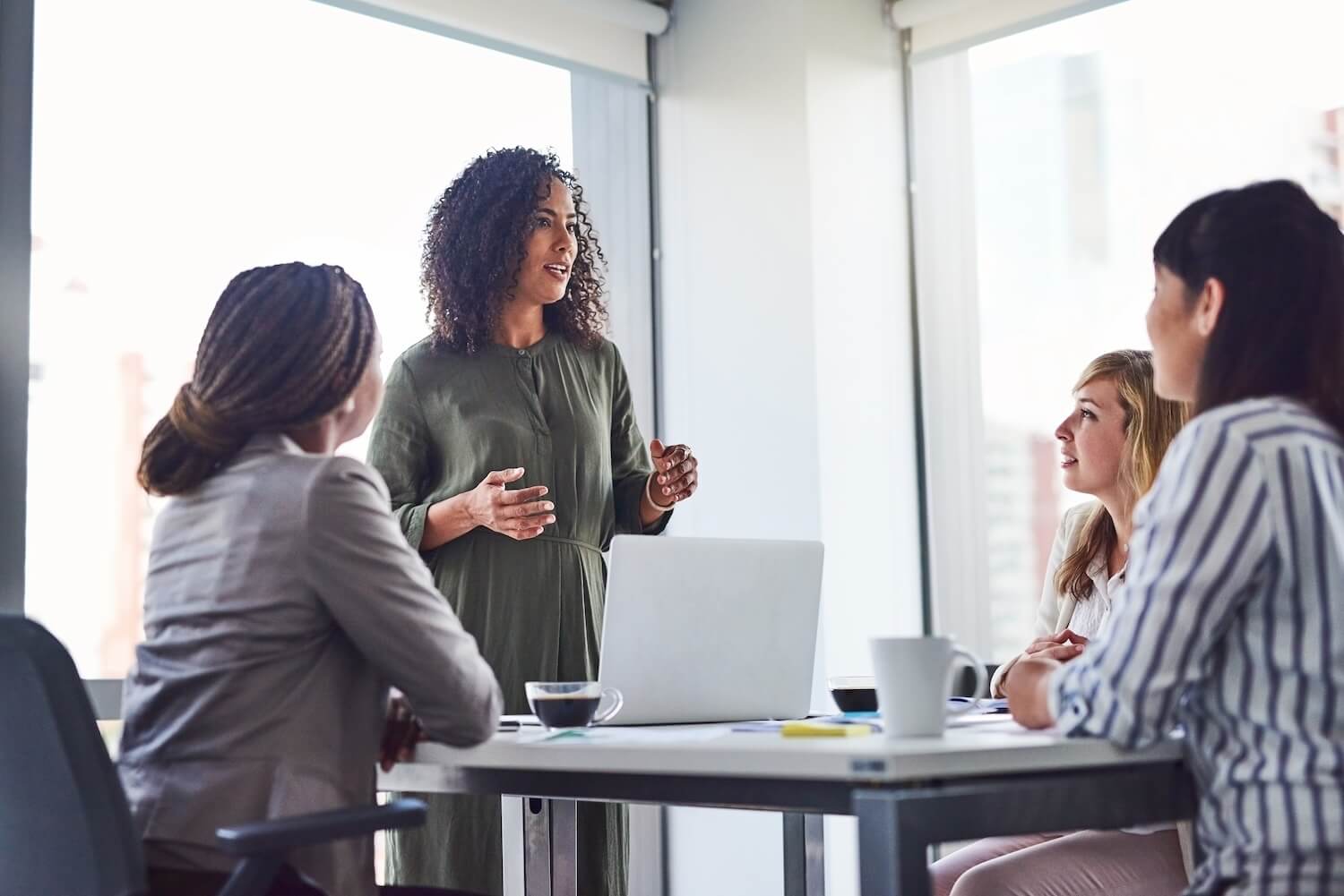 Top-Down vs. Bottom-Up: Teambesprechung mit einem Vortragenden, der spricht, während andere um einen Tisch herum sitzen, mit Laptops und Kaffeetassen.