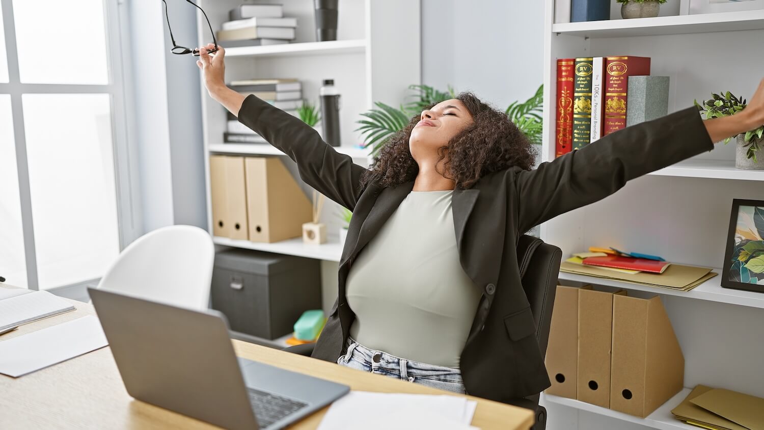 Resilience Coach strengthens stress management: woman stretching with relief at her desk, experiencing release after mental strain.