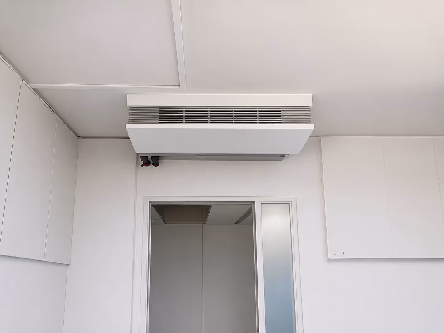 Weiße Decken-Klimaanlage montiert über einer offenen Tür in einem weißen Raum.