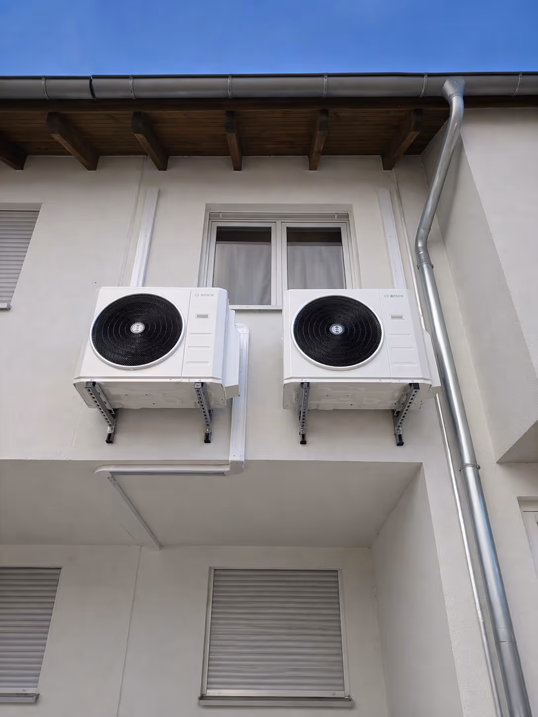 Zwei Bosch-Klimageräte sind an der Außenwand eines weißen Hauses unter einem Fenster montiert.