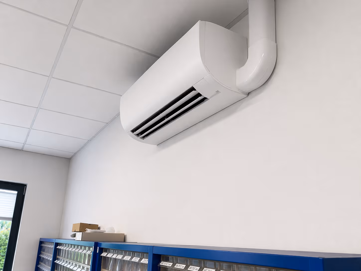 Moderne weiße Klimaanlage an einer weißen Wand über blauen Lagerregalen in einem Büro.